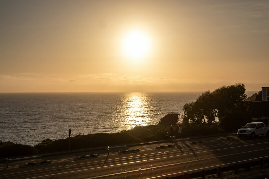 Convertible car driving on a coastal road at sunset